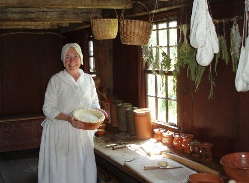 Baking at Daggett Farm Woman holds a pie in a rudimentary kitchen