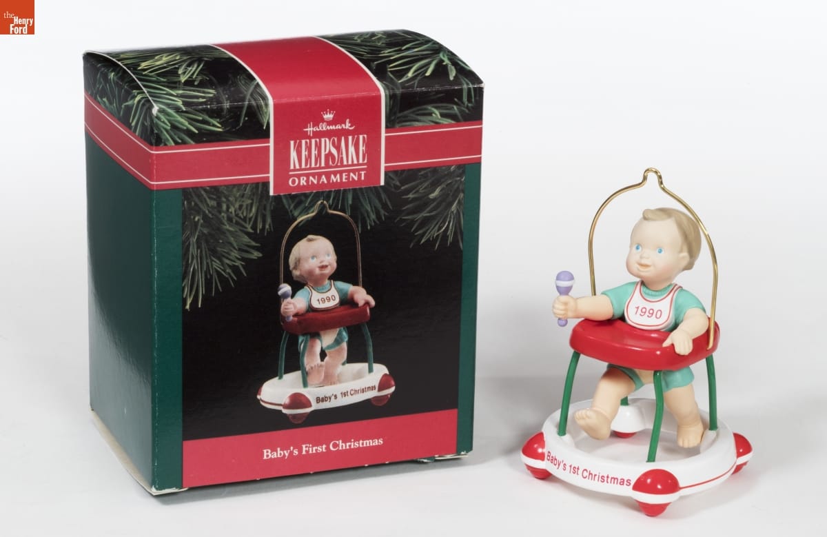 Hallmark "Baby's First Christmas" Christmas Ornament, 1990 Ornament with a baby or toddler in a walker with "Baby's 1st Christmas" written on it and "1990" on a bib around the baby's neck; it sits next to a green and red box with an image of the same ornament on it