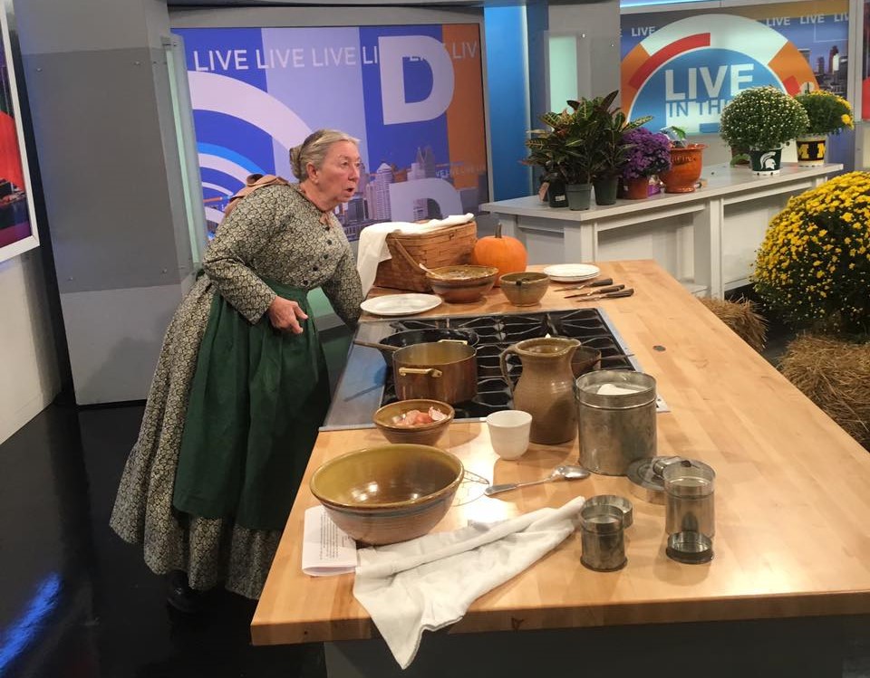 Cindy Melotti frying pumpkin fritters on the set of Live in the D Woman in old-fashioned dress and apron cooks on a television soundstage