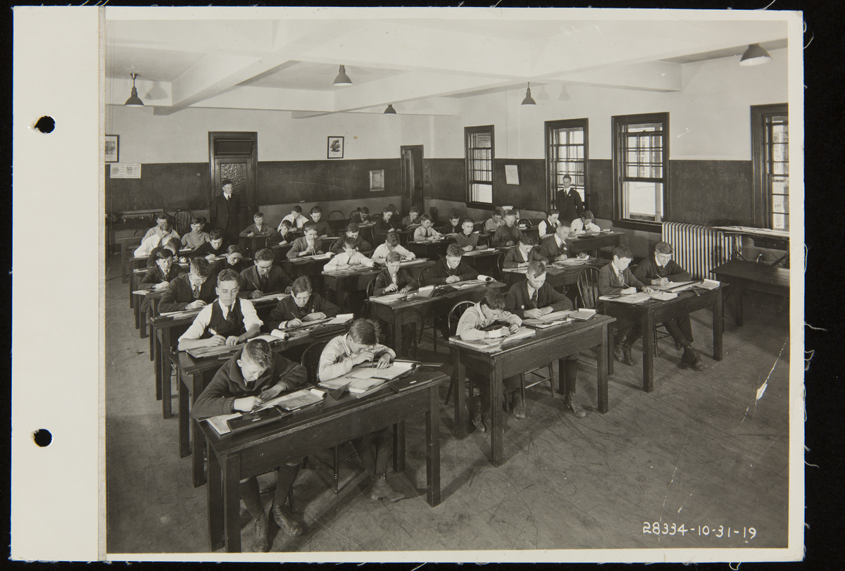 Henry Ford Trade School Students and Teachers in Classroom, October 31, 1919 Group of students work at desks in a classroom with a teacher standing in the back
