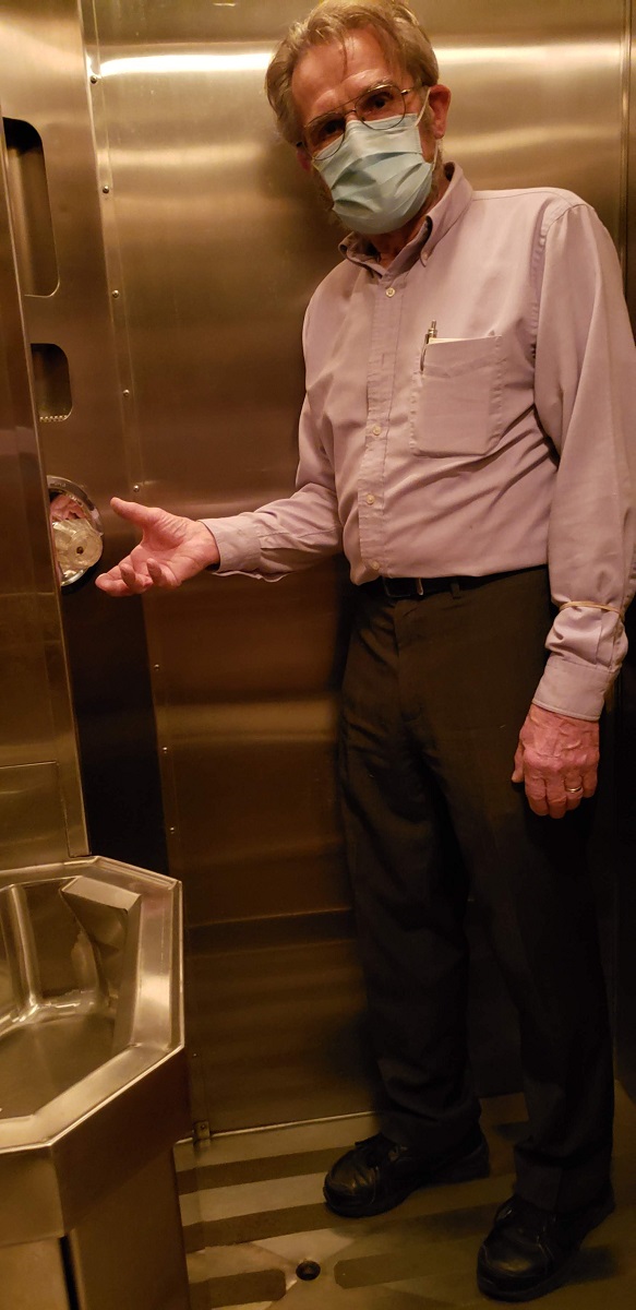 Photographer Rudy Ruzicska in the bathroom of the Fair Lane railroad car Man stands with hand next to knob in a stainless steel restroom containing a sink