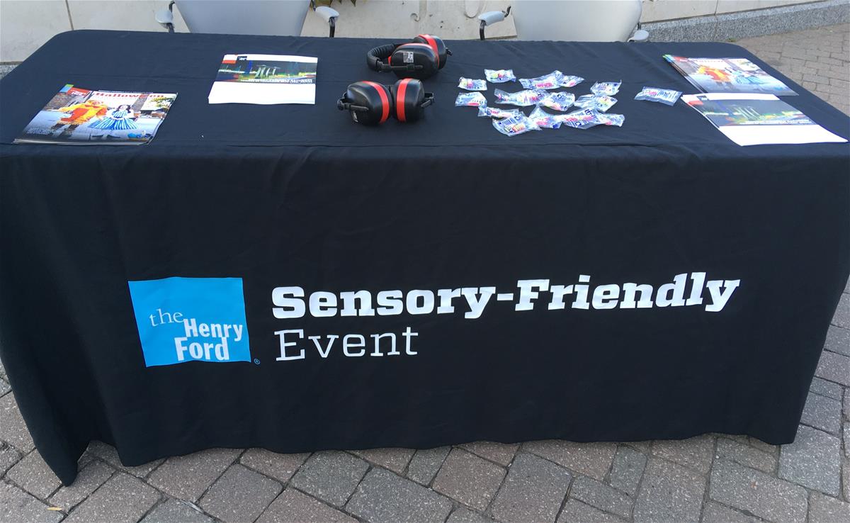 Sensory-Friendly Event Entrance Table Table covered in black cloth with text "Sensory-Friendly Event" and brochures and headphones on top