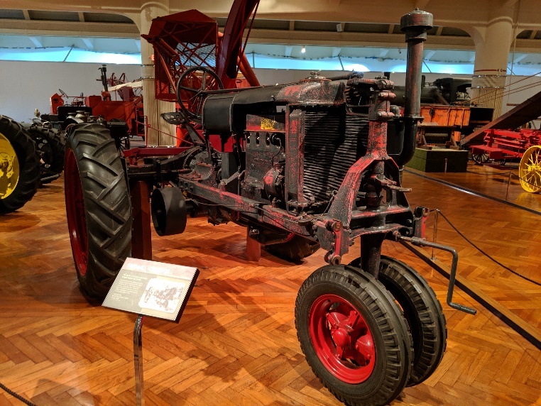 Tractor on wood floor in exhibit, surrounded by other equipment