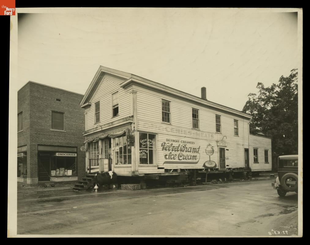 J.R. Jones General Store (Just Before the Move to Greenfield Village), Original Site, Waterford, Michigan, 1926 Two story wooden building with mural on side, elevated slightly on jacks