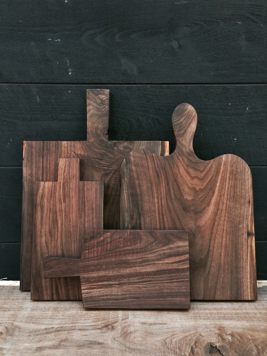 Examples of Patrick Moore's cutting boards, featuring wood with unusual grain Four wooden cutting boards of different sizes, leaning against a dark gray wooden wall