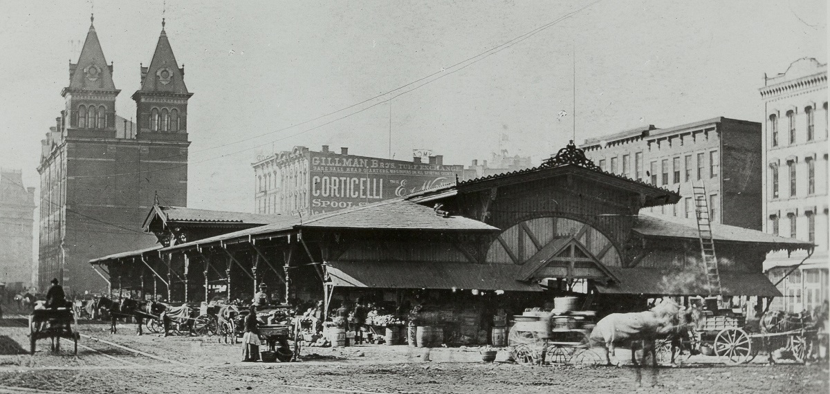 Detroit Central Market, circa 1888 Black-and-white photo of long, low, open building with people and horses and carriages around it