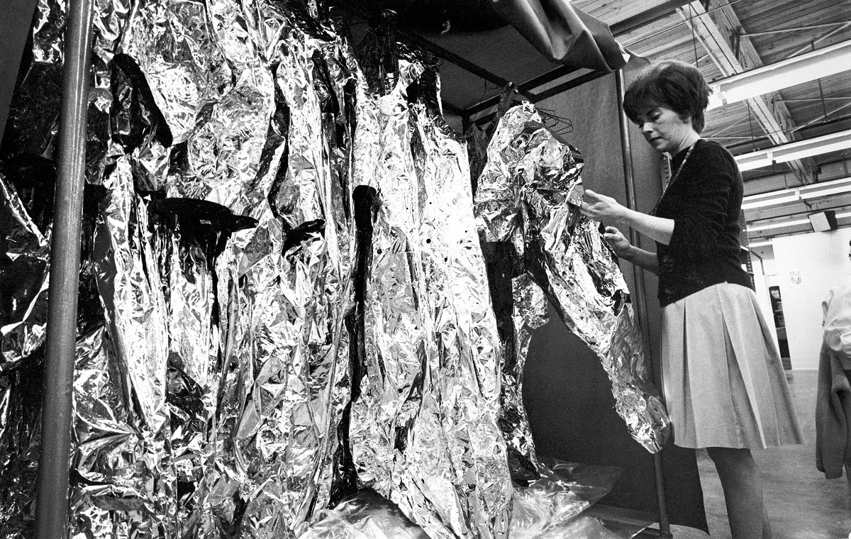 Arlene Thalene working on spacesuits at ILC Dover Woman examines a thin mylar suit hanging in a rack of similar suits