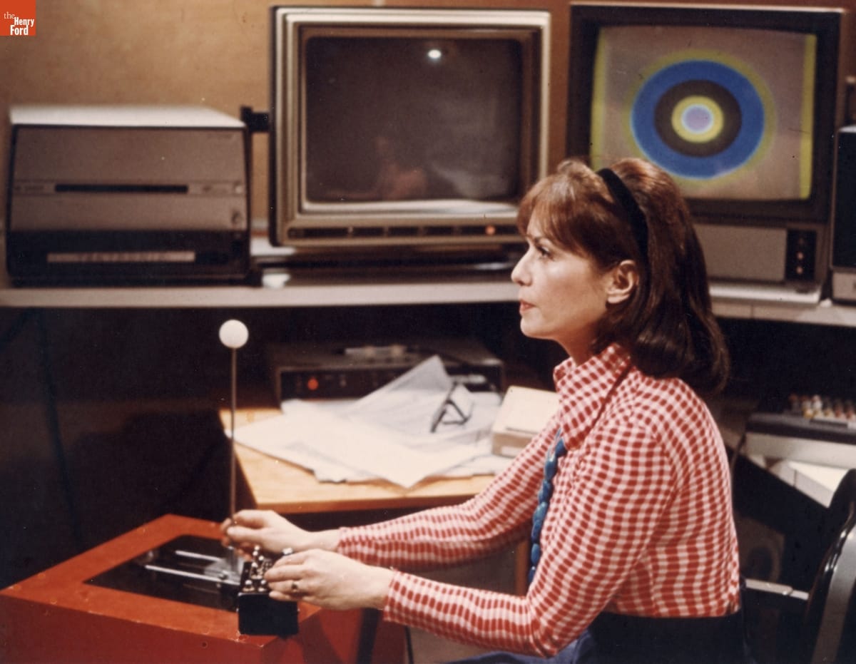 Lillian Schwartz at Work, Bell Laboratories, circa 1975 Woman in red-checked shirt surrounded by monitors and other computer peripherals manipulates a joystick device while looking straight ahead