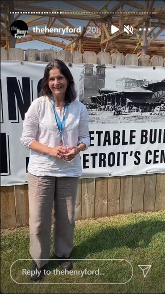 Debra A. Reid, Curator of Agriculture and the Environment at The Henry Ford, by the Vegetable Building construction site in Greenfield Village Woman in tan slacks and white shirt with lanyard around neck stands outside a wooden fence, behind which a building is partially erected