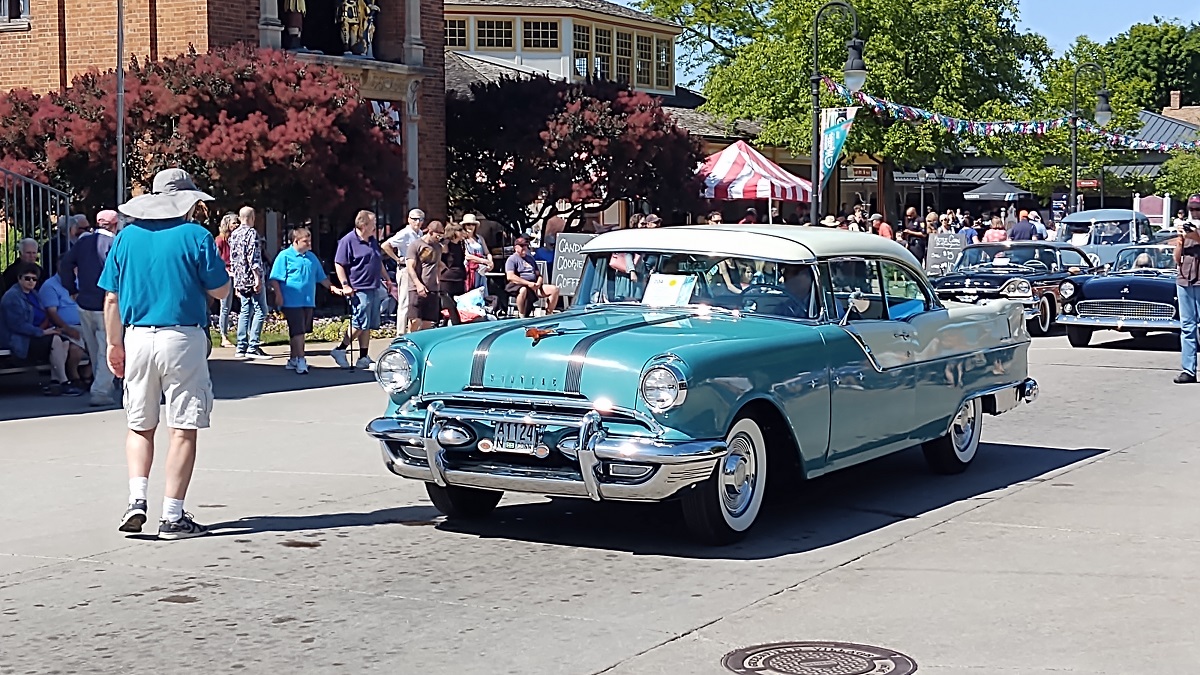 A 1955 Pontiac Star Chief at pass-in-review during Motor Muster 2022 A turquoise and white 1950s vehicle on a road with onlookers and other vehicles nearby