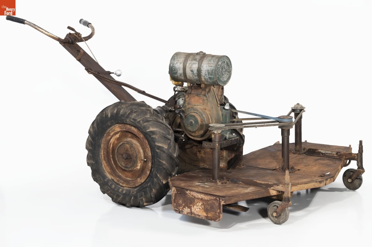 Prototype Walking Tractor with Tri-Cut Mower, circa 1956 Rough lawnmower with flat attachment and two small wheels in front; two large wheels behind; and crude handlebars