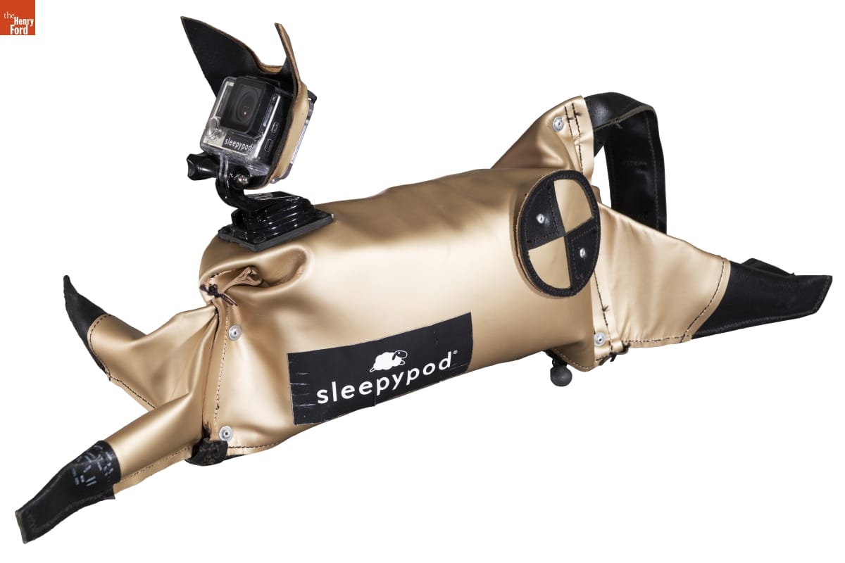 Sleepypod "CLEO" Crash-Test Cat, 2015 Champagne-colored fabric or plastic cat figure, with text and circular shape on side and camera where face would be