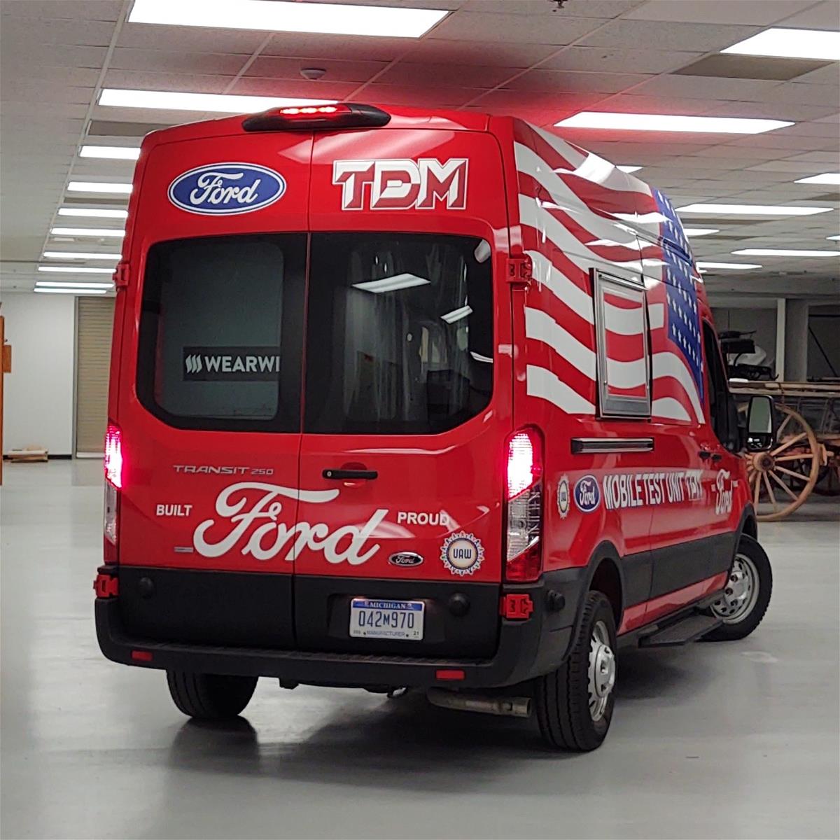 Rear view of red van with large back window; various text on vehicle and large American flag on visible side