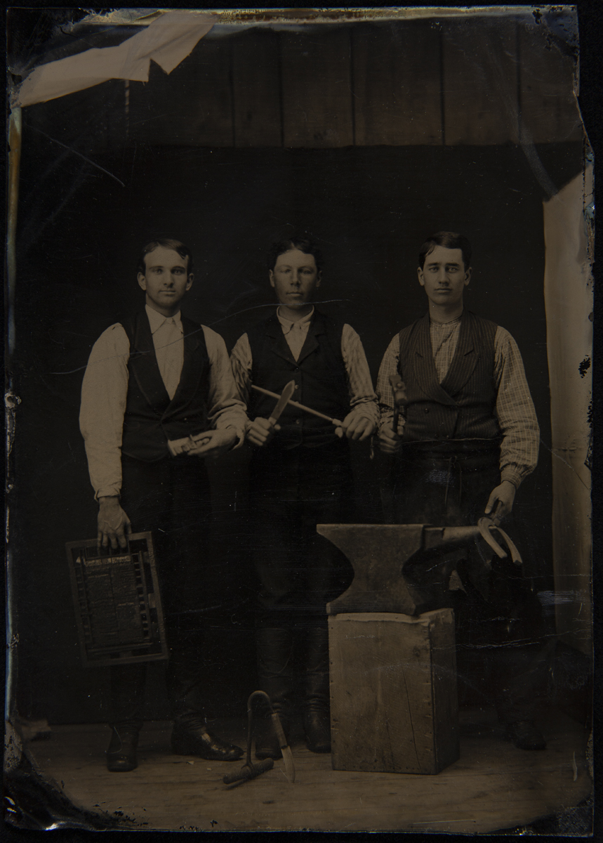 Typesetter, Butcher, and Blacksmith with their Tools, circa 1880 Three men in vests and shirtsleeves standing behind an anvil on a wooden block, holding tools