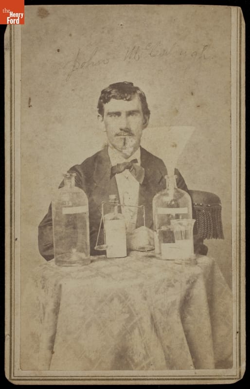 Portrait of John C. McCullough, M.D., Wheatland, Indiana, May 19, 1875 Black-and-white portrait of man in suit sitting at table containing bottles and jars