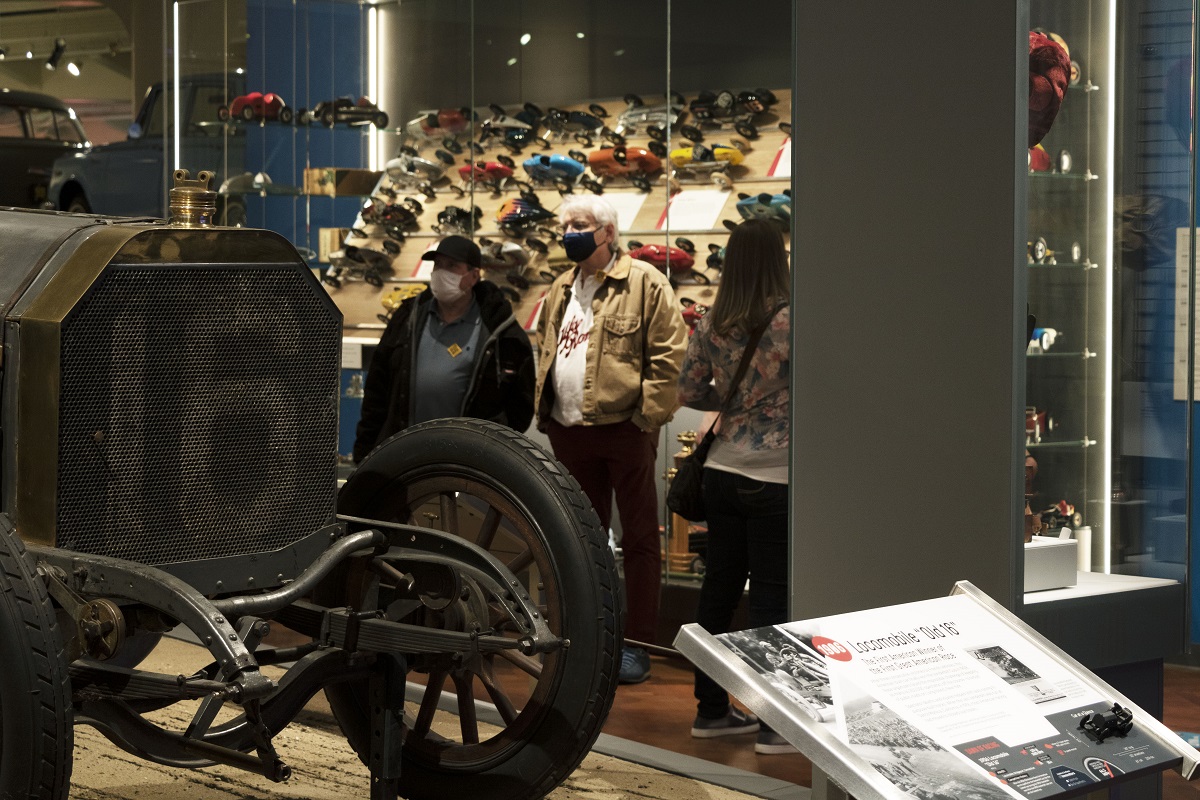 Guests check out the new Driven to Win exhibit over opening weekend Several people look at a museum exhibit, standing among display cases and cars