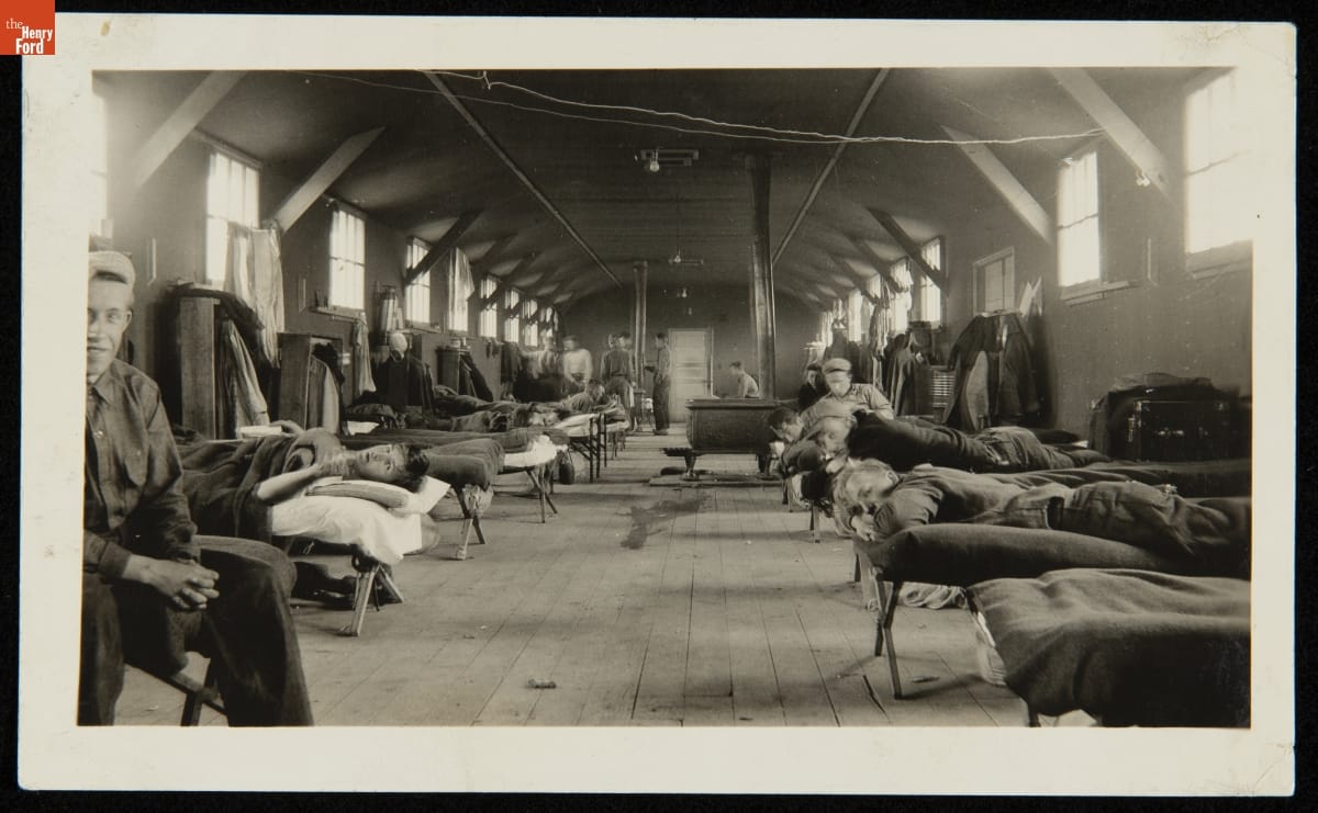 Interior of Civilian Conservation Corps Barracks, 1934 Interior of large wooden room with high windows filled with cots, some with men standing by, sitting on, or lying on them