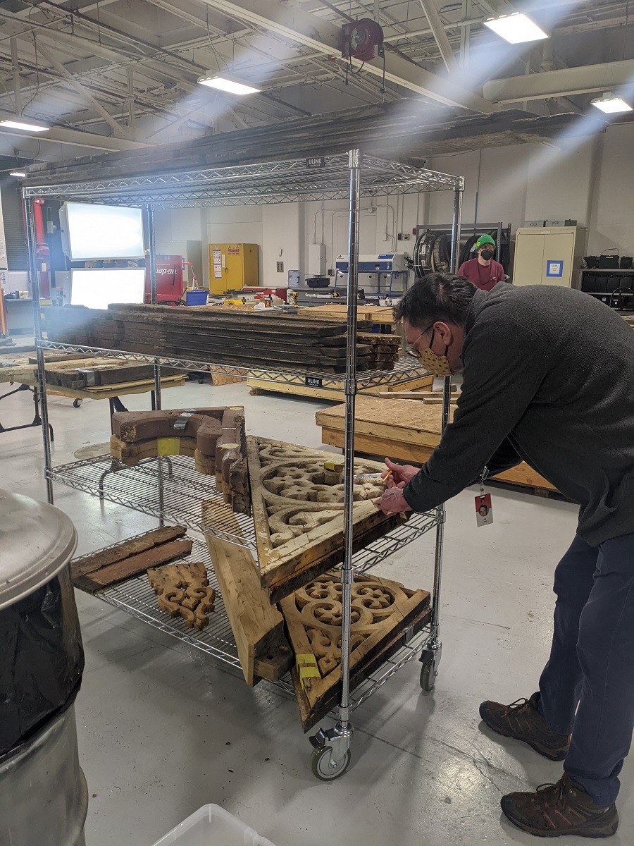 Jim Johnson inventorying architectural elements from the Detroit Central Market Man leans over wooden architectural elements on metal shelving in a large, sunny warehouse space
