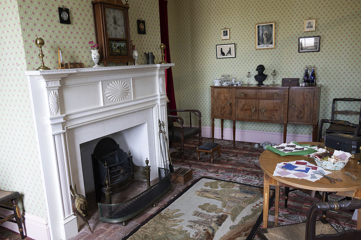 Part of carpeted and wallpapered room showing fireplace, sideboard, table and chairs