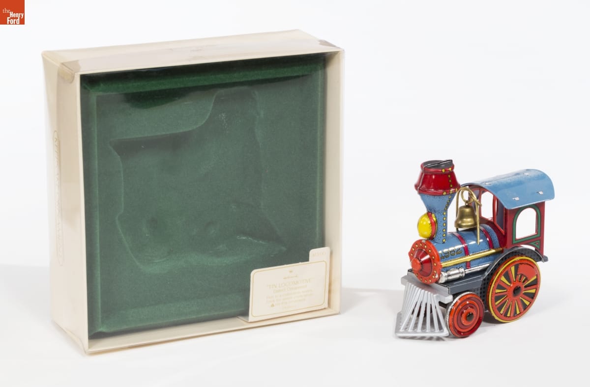 Hallmark "Tin Locomotive" Christmas Ornament, 1982 Colorful ornament of a blue steam locomotive sits next to a cream-colored box with green velvet insert and clear plastic top