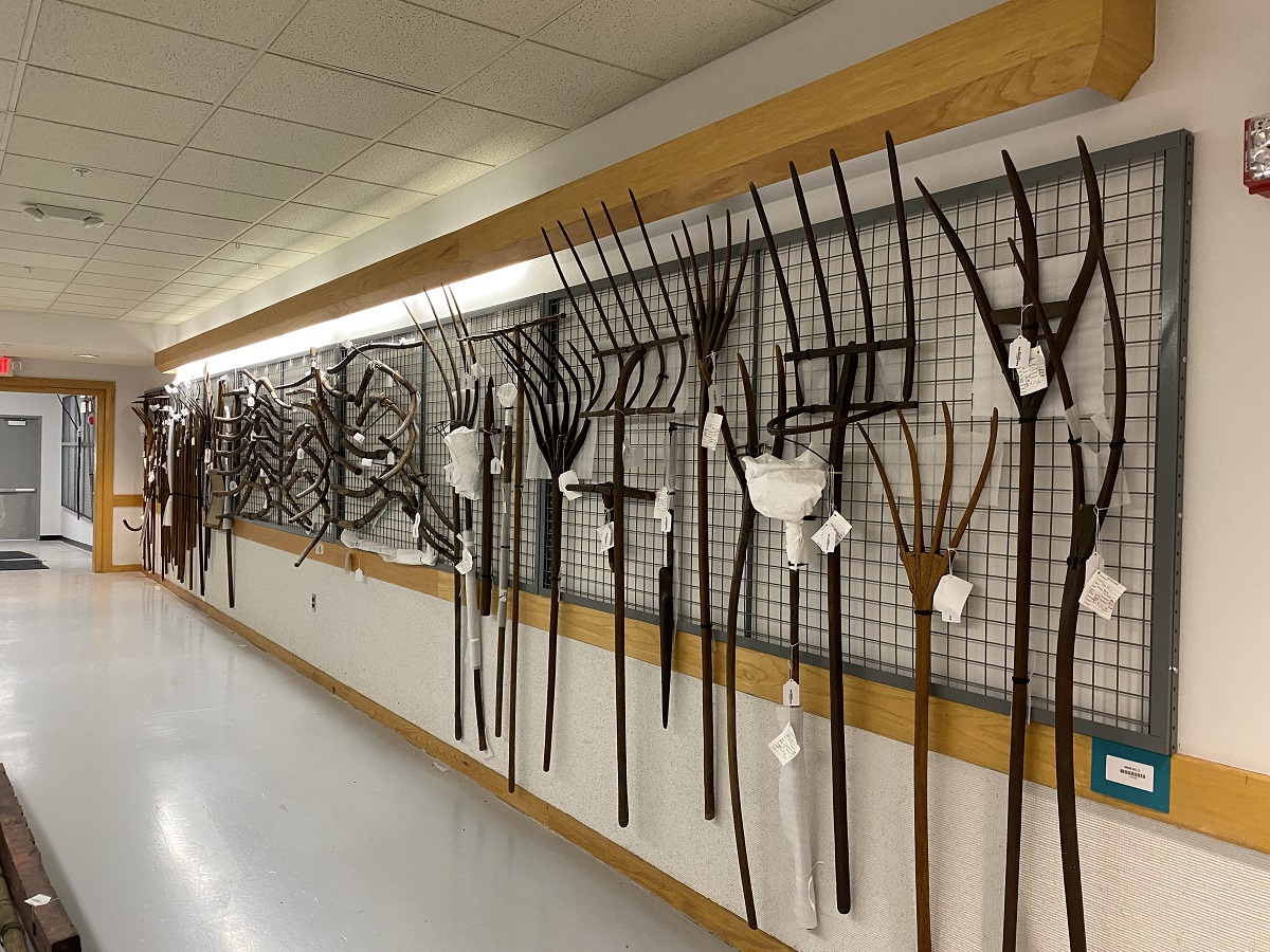 Agricultural implements hang from a wire grid within MSB Wooden rakes, yokes, and other items hang from a wire grid in a hallway