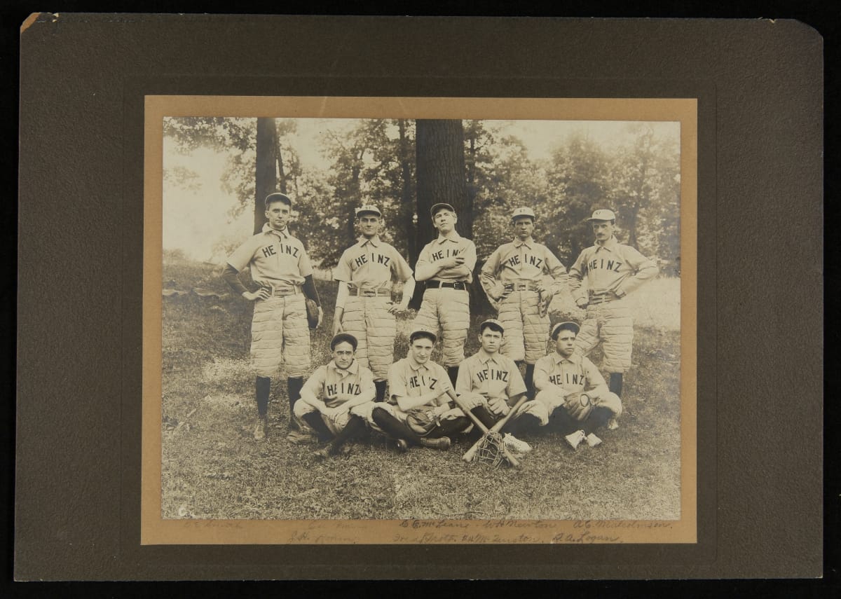 H.J. Heinz Company Baseball Team, circa 1907 Black-and-white photo of five men standing, four men sitting, some with gloves and bats, wearing baseball uniforms and caps