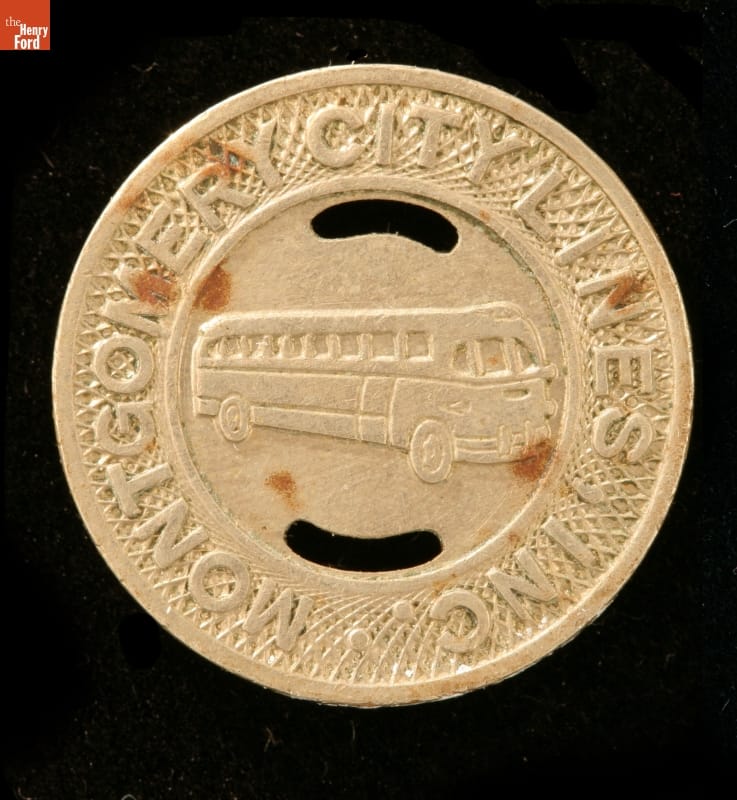 Round gold-colored token with text around outside and picture of bus in center