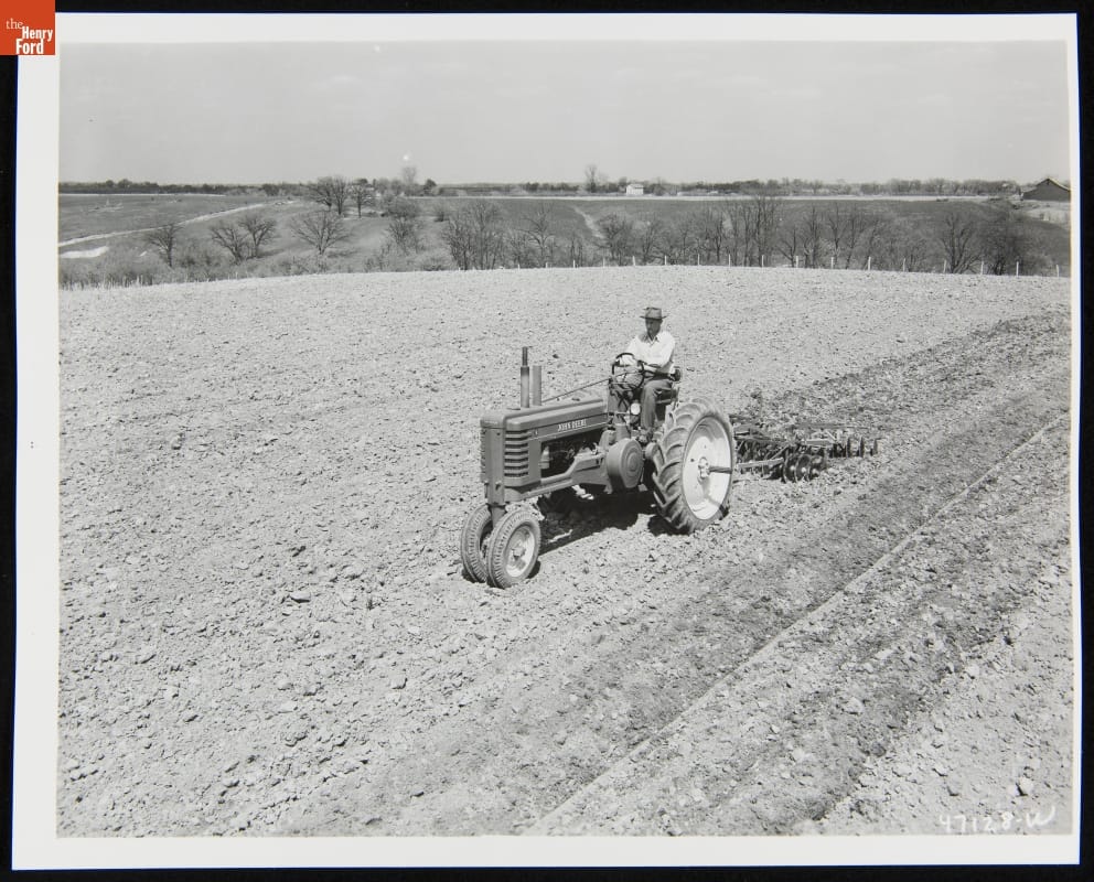 Man Using a 1947-1952 John Deere Model "B" Series Tractor Black-and-white photo of man riding a tractor through a dirt field