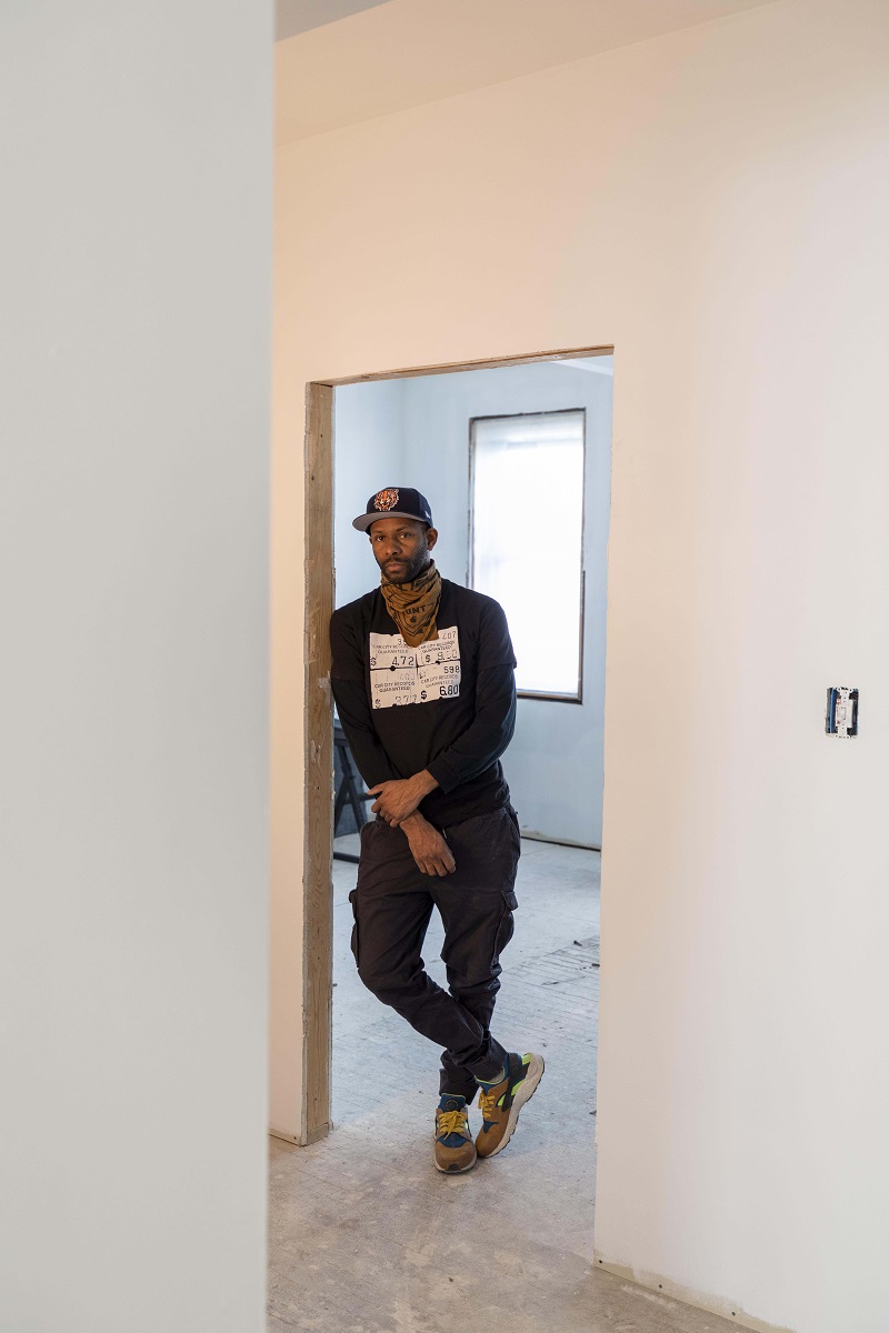 Wajeed African American man leans in the doorway of an empty room that appears to be under construction