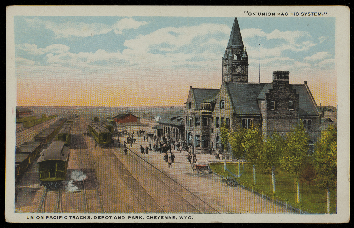"Union Pacific Tracks, Depot and Park, Cheyenne, Wyoming," 1908-1910 Postcard depicting large stone building with clocktower next to railroad tracks; people stand on platform between