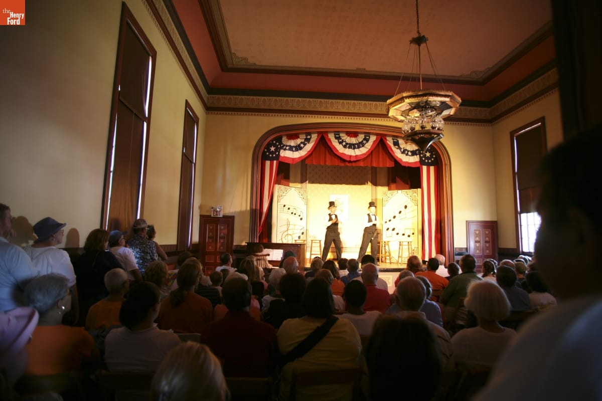 Ragtime Street Fair in Greenfield Village, July 2007 / Photographed by Michelle Andonian Two people on a stage surrounded by red, white, and blue bunting perform in an auditorium filled with people