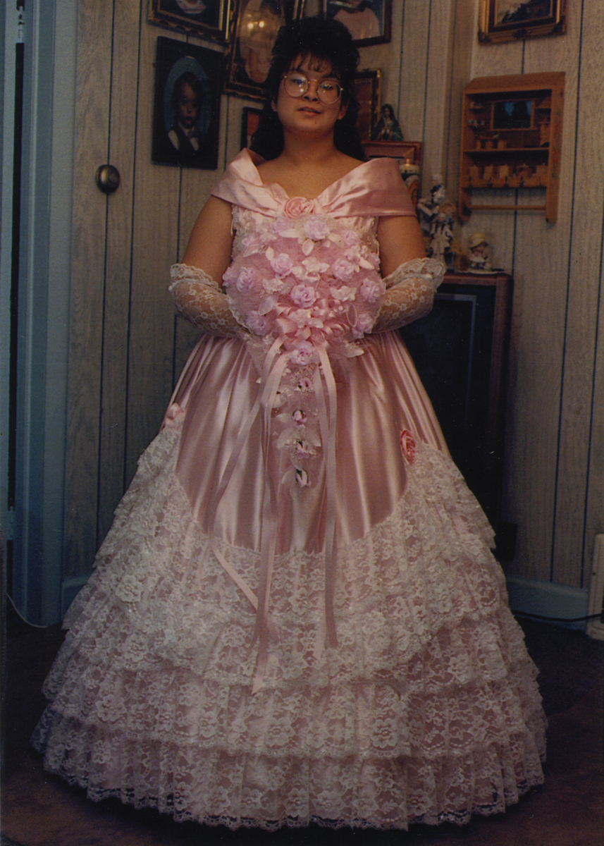 Woman with long dark hair and glasses wearing pink gown with tiers and white lace holds an elaborate flower arrangement