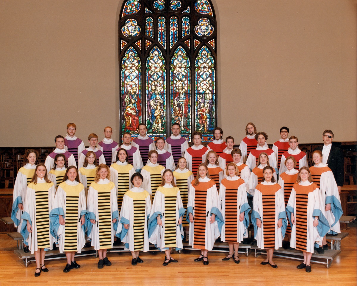 Hope College Chapel Choir at Dimnent Chapel, circa 2001 Group of people in colorful robes with black stripes, standing on bleachers in front of a stained glass window