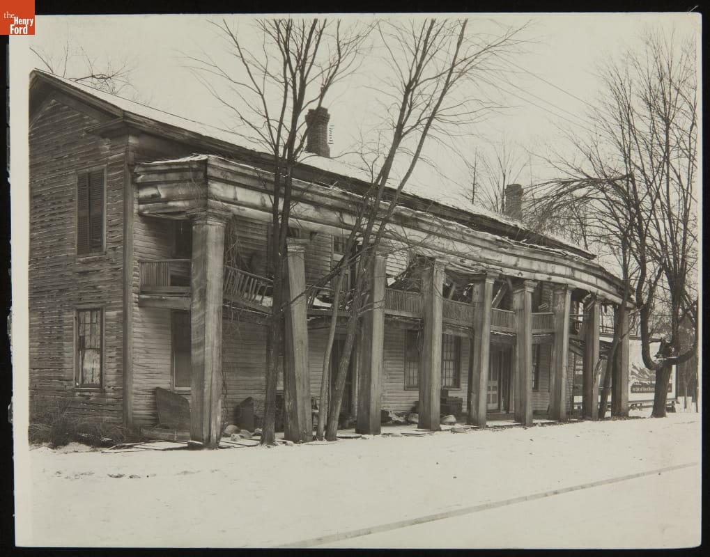 Eagle Tavern at Its Original Site, Clinton, Michigan, 1925 Decrepit two-story wooden building with columns in front, leaning at different angles, and second-floor balcony that is sagging