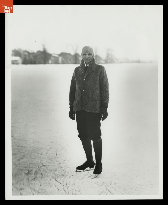 Henry Ford Ice Skating, 1918 Man in cardigan with collar turned up, hat, knickers, and ice skates, on ice with trees and buildings in background
