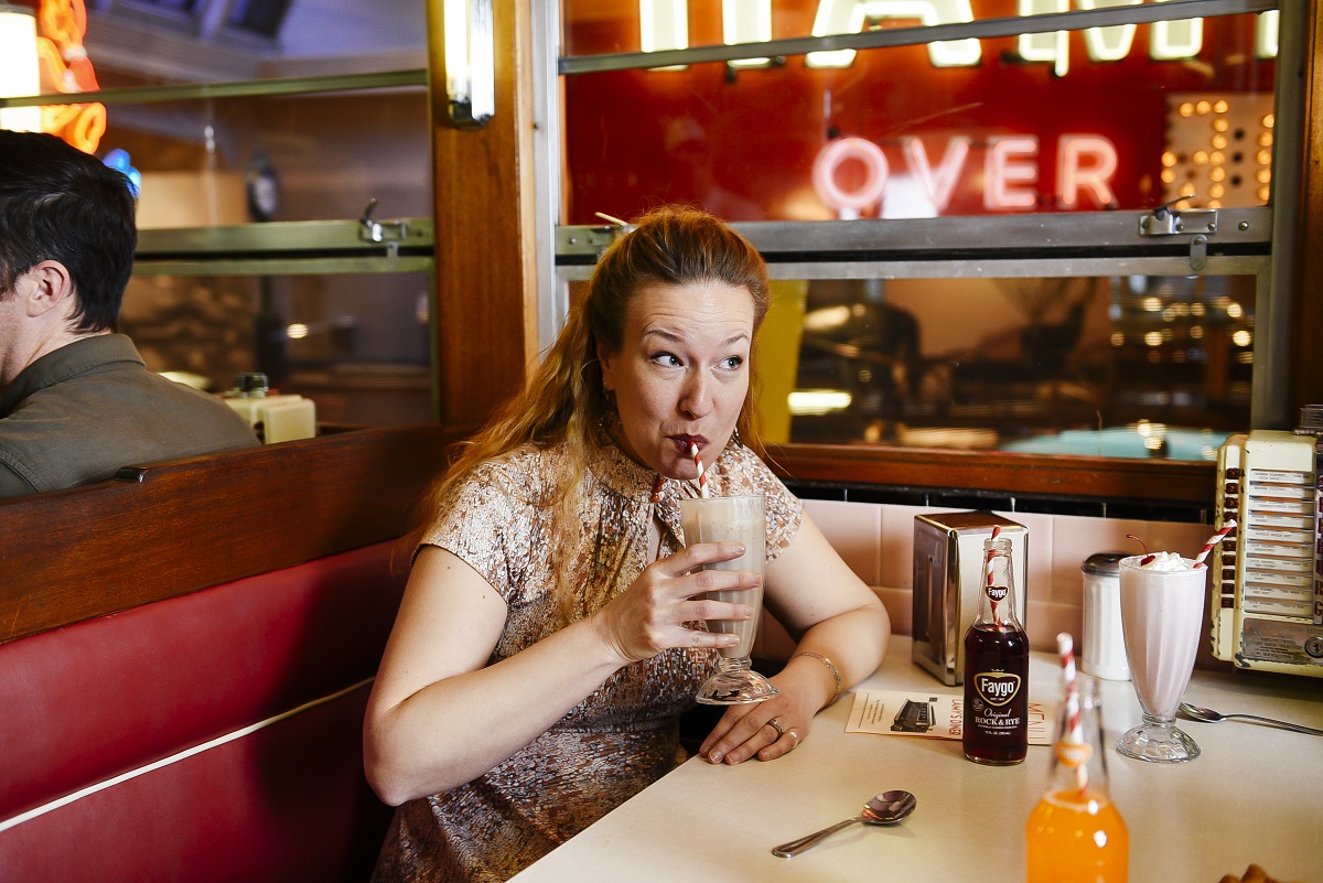 Enjoying a frappe at Lamy's Diner Woman sits in diner booth and sips a milkshake from a straw