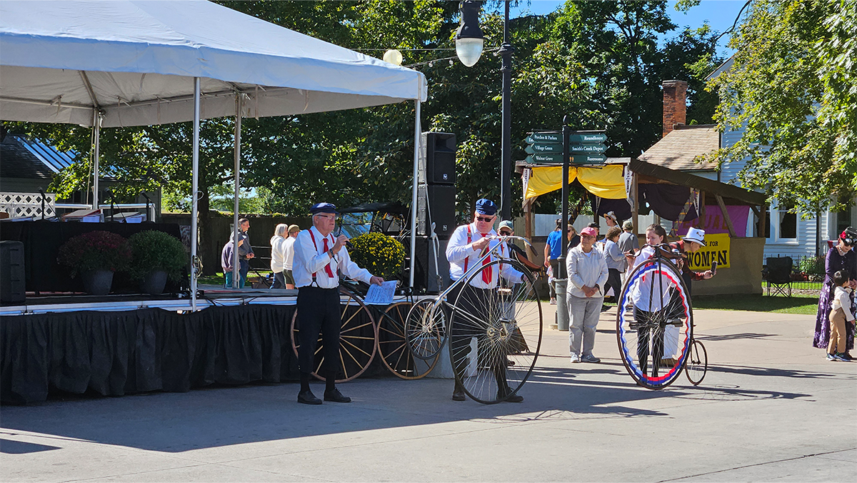 3 men in white shirst in front of a stage, standing next to big wheel bicycles
