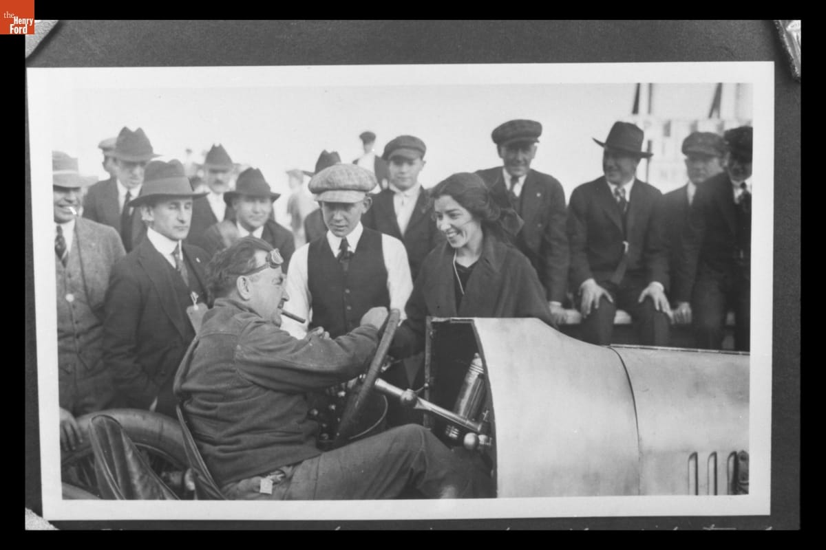 Katherine Stinson with Barney Oldfield at Ascot Speedway, Los Angeles, California, November 29, 1917 Crowd of men and one woman gathered around man with cigar sitting in open race car
