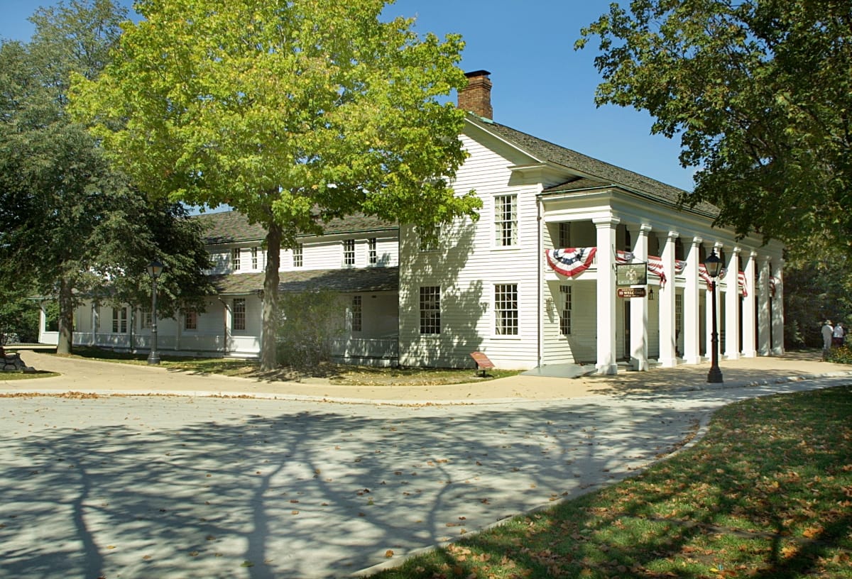 Eagle Tavern in Greenfield Village Large, two-story white wooden building with columns and second-floor balcony, among trees